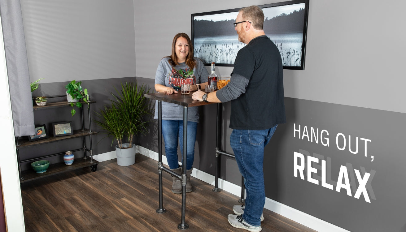 Two people enjoying drinks at a DIY pipe bar table in a cozy industrial-style room.