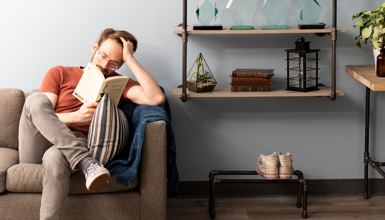 Person reading a book on the couch in a small living room setting adorned with pipe shelves, pipe shoe rack, and a pipe side table.