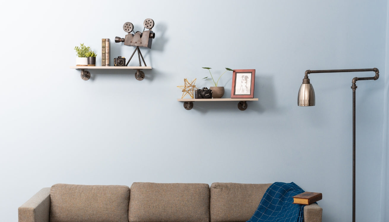 Wall-mounted floating pipe shelves styled with books, plants, and decor above a beige couch and next to an industrial pipe floor lamp.