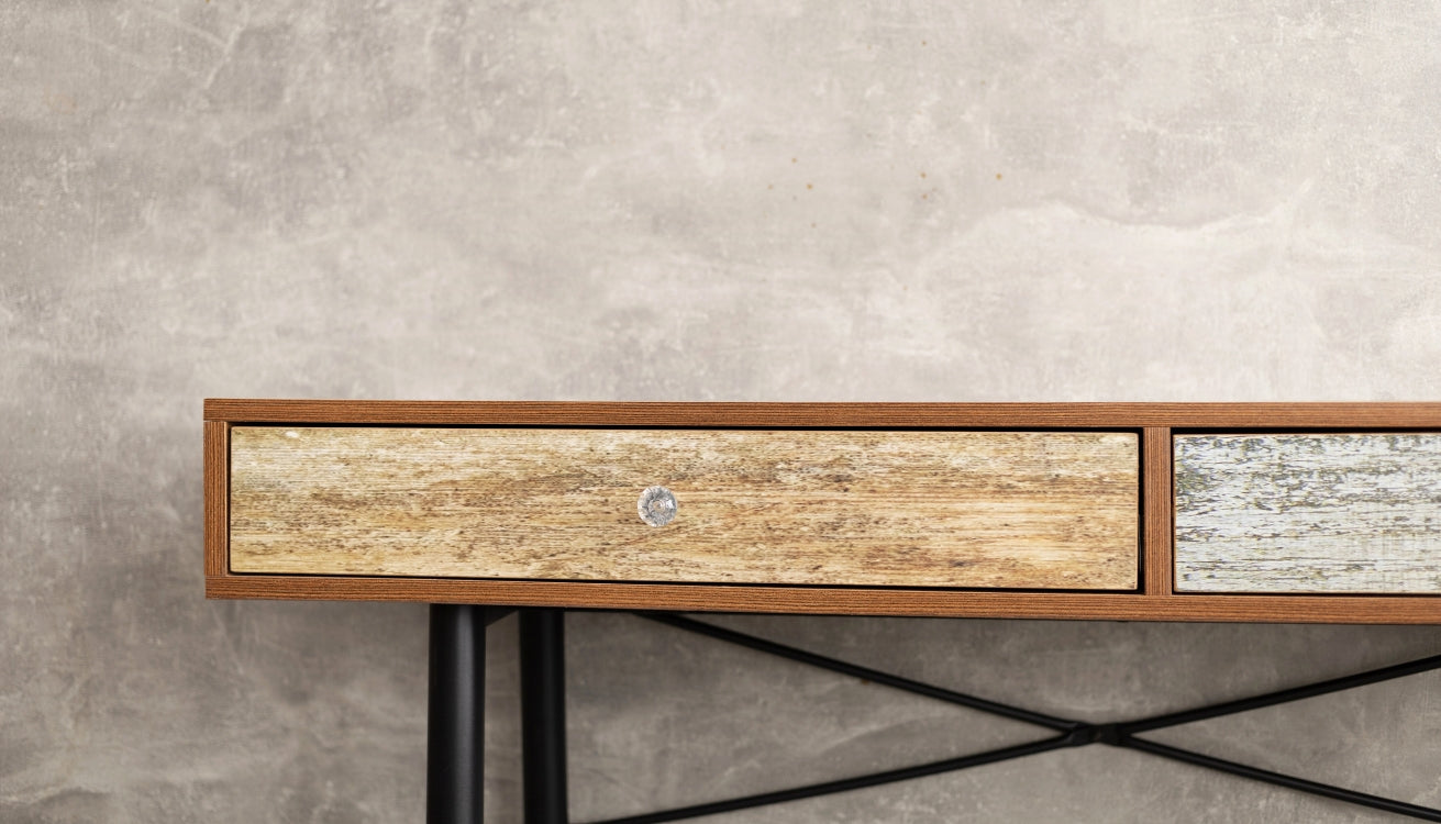 A close-up of a rustic wooden console table with mixed wood finishes, featuring sleek black legs and a minimalist design, set against a textured concrete wall.