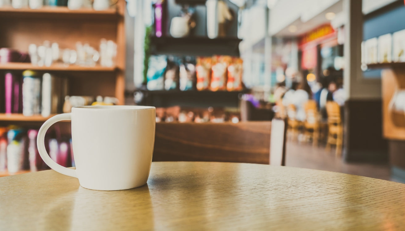 White mug on a wooden table in a cozy coffee shop with a warm coffee shop aesthetic. 