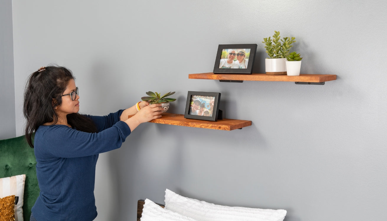 Image of a woman arranging potted plants and family photos on wooden PIPE DECOR® shelves, a thoughtful Mother's Day gift enhancing her home décor.