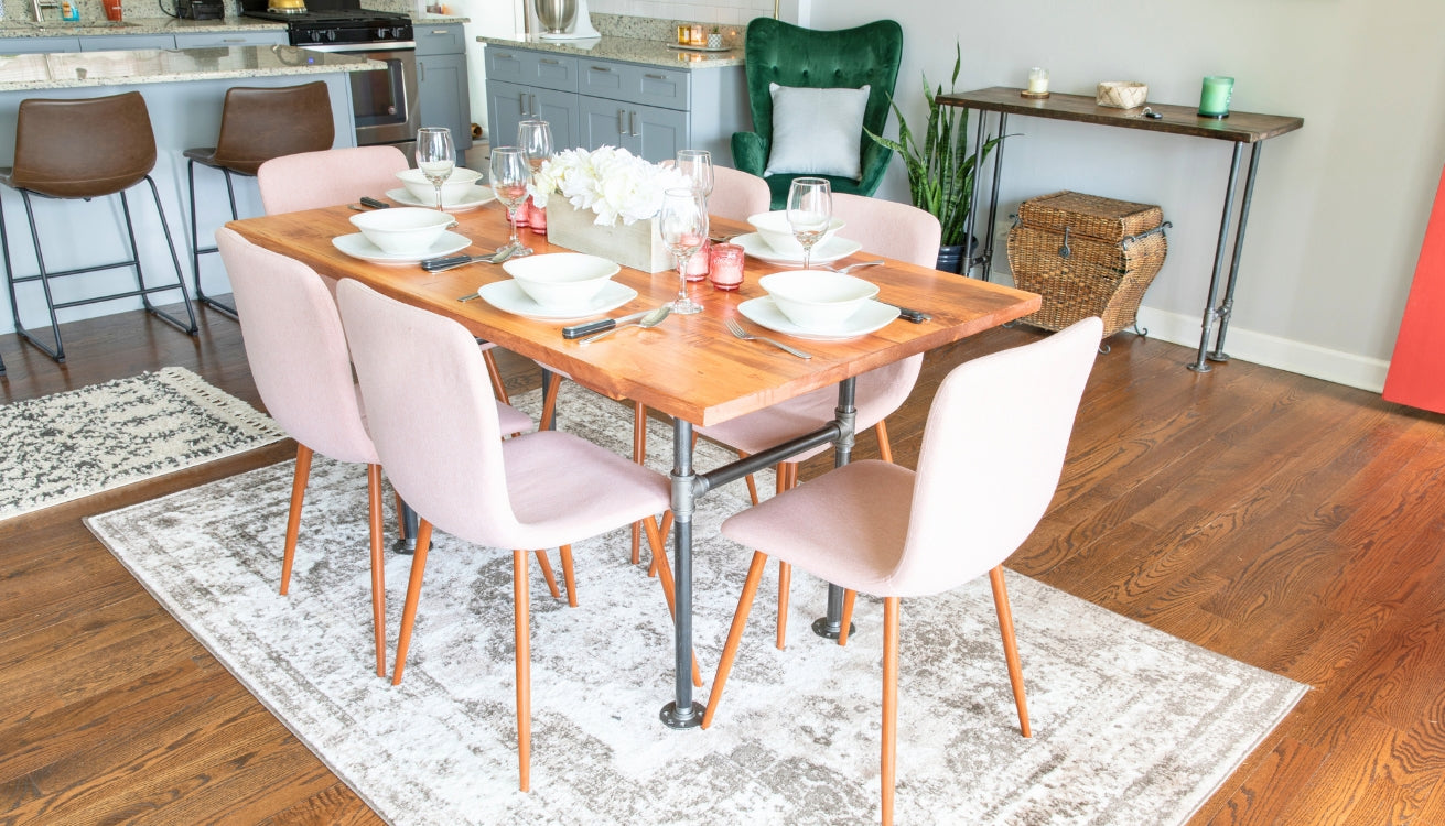 Industrial pipe dining table with a wooden top and six modern pink chairs, set in a contemporary dining area with additional industrial pipe furniture and decor.