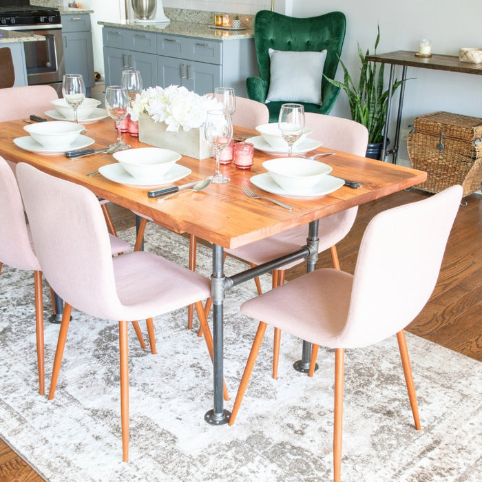 Industrial pipe dining table with a wooden top and six modern pink chairs, set in a contemporary dining area with additional industrial pipe furniture and decor.