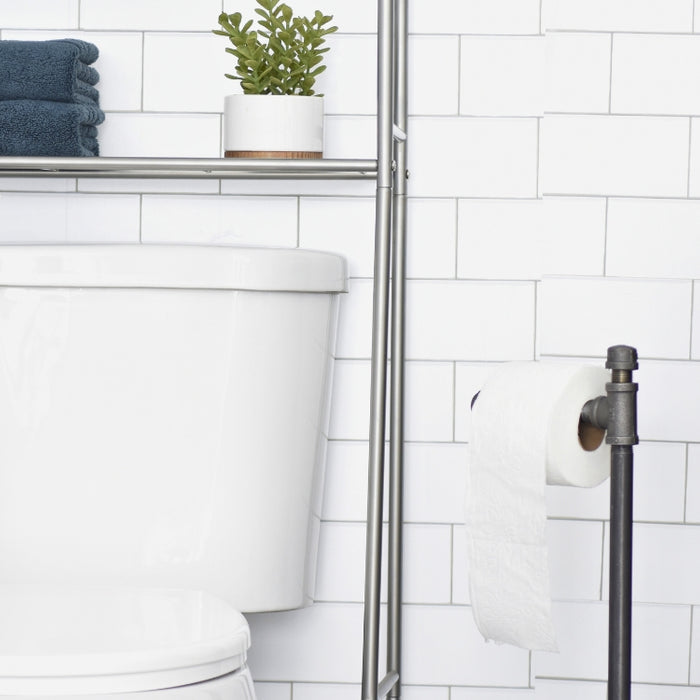 Freestanding industrial pipe toilet paper holder in a modern bathroom with white subway tiles and minimalist decor.