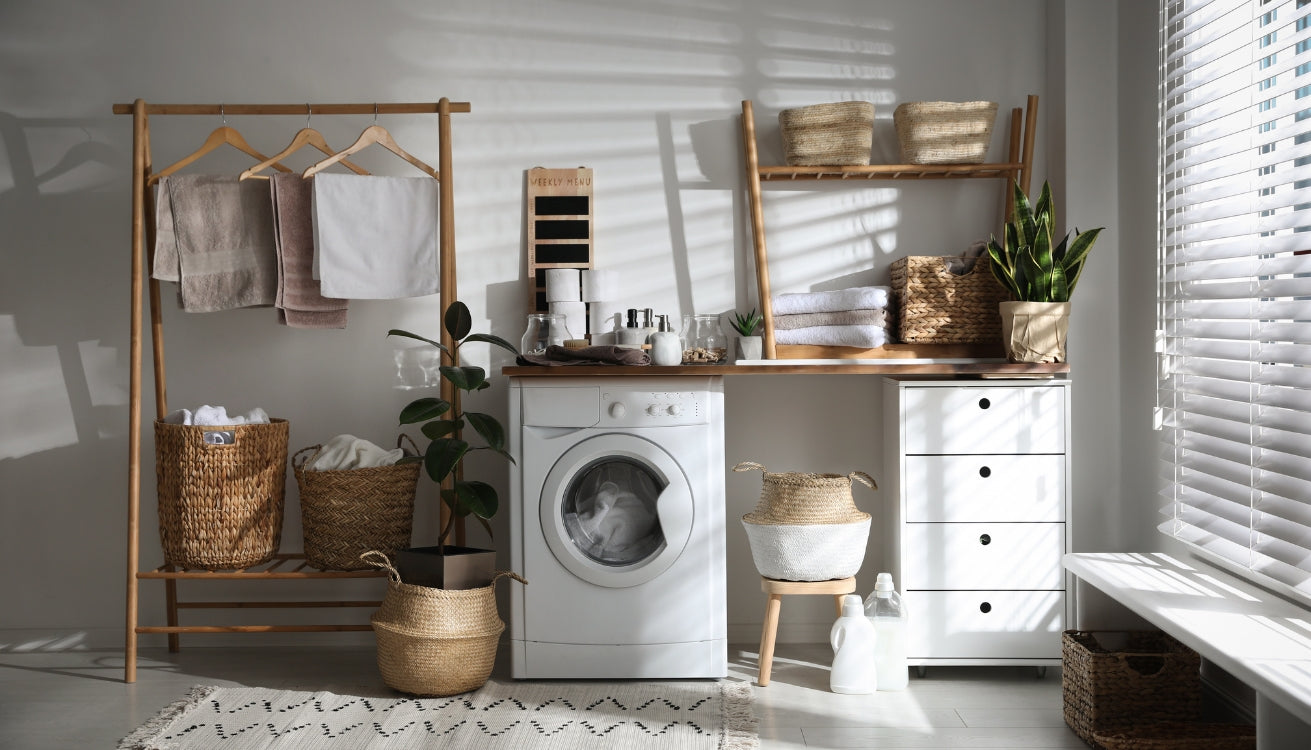 A bright and organized stacked laundry room with wooden shelving, baskets for storage, a white washing machine, and a potted plant adding a touch of greenery. 