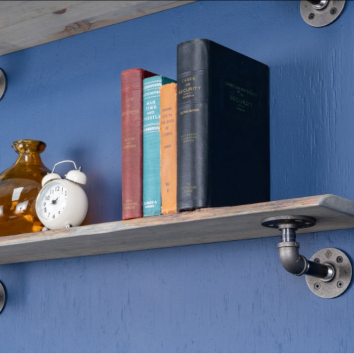 Industrial pipe shelf mounted on a blue wall, styled with books and decor items including a vintage clock and a glass vase.