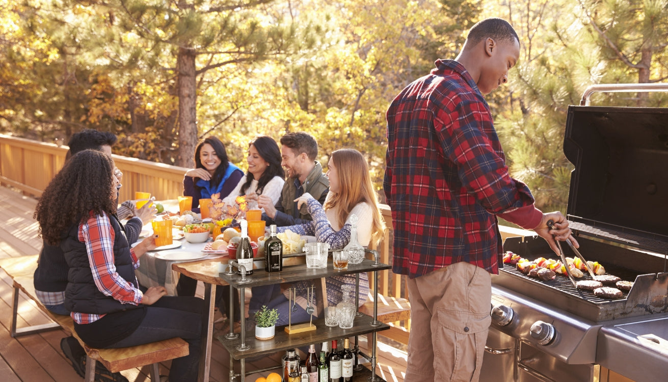 A group of friends celebrating memorial day outside cooking barbecue with drinks served on a pipe bar cart. 