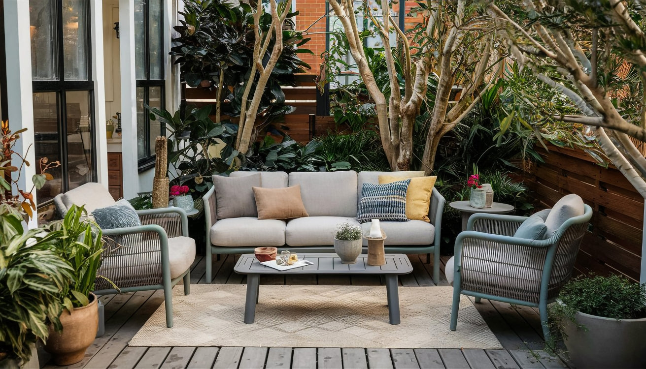 A cozy small patio setup with gray outdoor furniture, surrounded by lush green plants, creating a serene and inviting outdoor retreat.