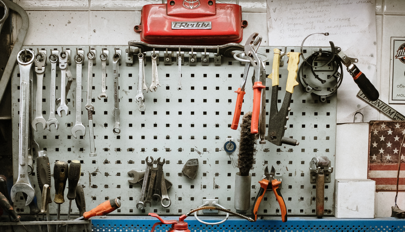 Collage of clever DIY storage solutions for the garage, including pegboard walls, custom shelving units, ceiling-mounted storage racks, industrial pipe clothing rack, repurposed old furniture, pipe bike rack, and DIY workbench by PIPE DECOR.