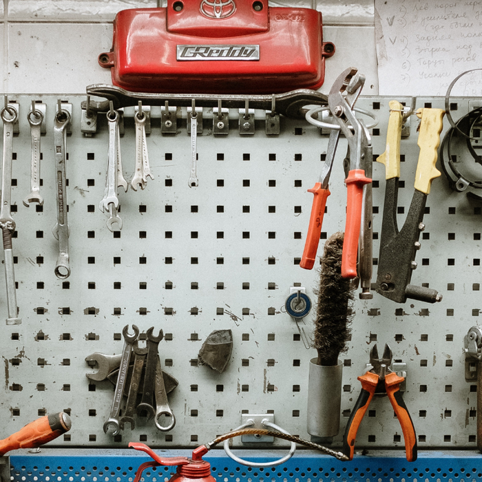 Collage of clever DIY storage solutions for the garage, including pegboard walls, custom shelving units, ceiling-mounted storage racks, industrial pipe clothing rack, repurposed old furniture, pipe bike rack, and DIY workbench by PIPE DECOR.